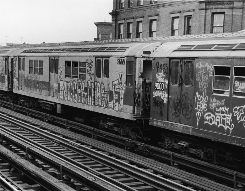 A black and white photo of subway cars with graffiti.