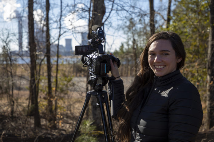 women in wooded area smiling next to video camera