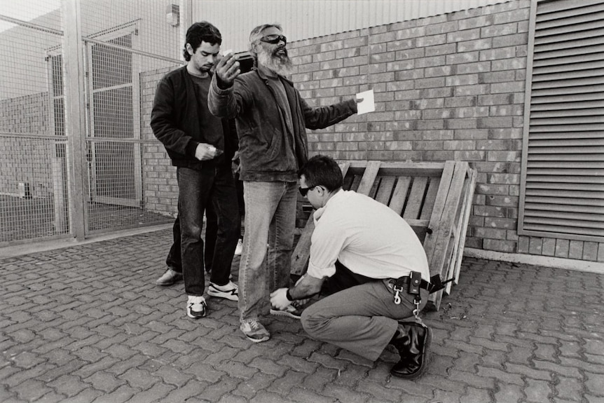 a black and white photo of prisoners being checked by a guard.