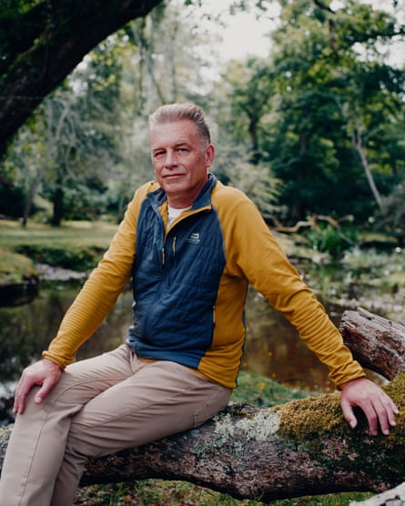 Chris Packham sitting on a log by a lake