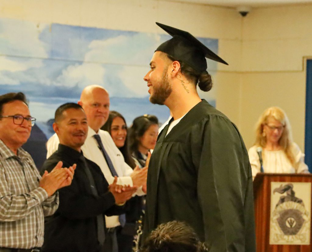 Man wears cap and gown while others clap.