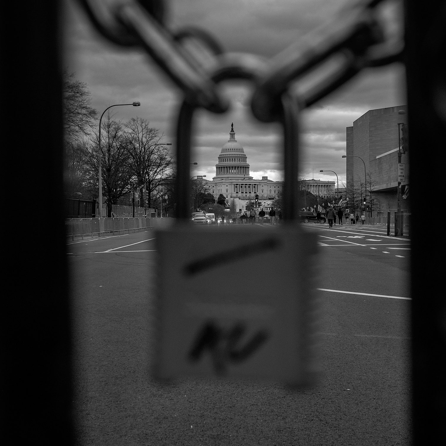 A blackandwhite photograph of the U.S. Capitol seen through a gate and padlock.