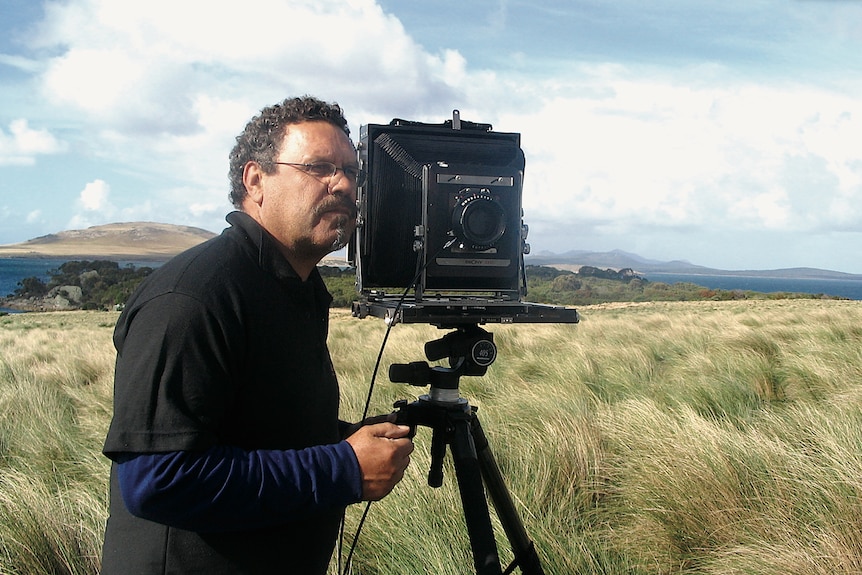 A man looking into a camera on a tipid in a field