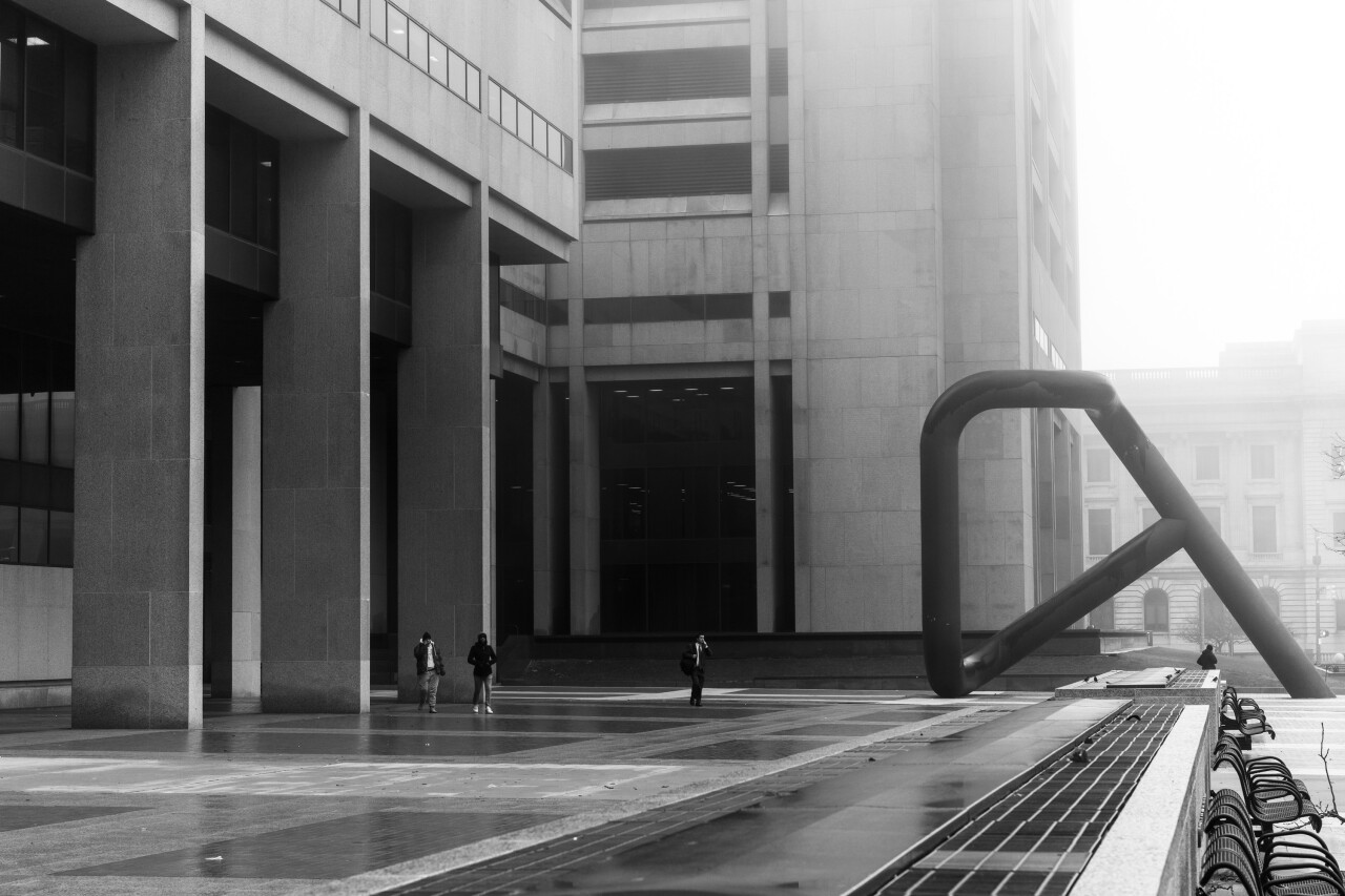 A black and white photo of people walking by buildings on a foggy day. 