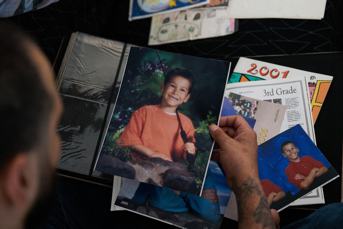 A man with tattoos looks at a school photo of himself as a child, smiling and posing with a fishing pole. 