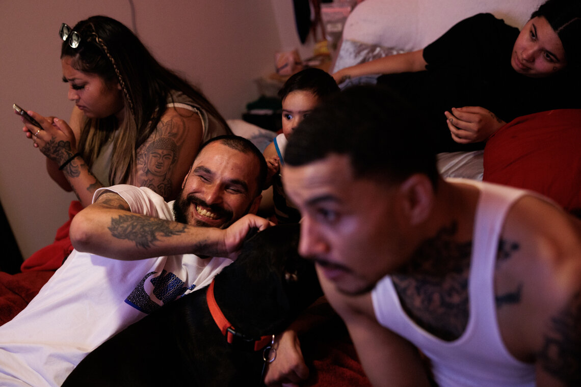 A man with a beard smiles while petting his dog, surrounded by his relatives. 