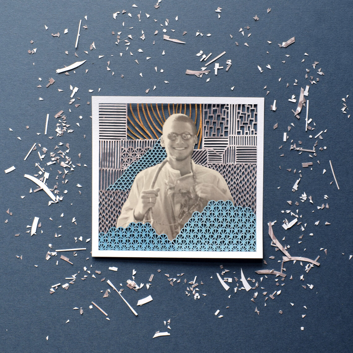 A yearbook photo of Leon Jacob, a White teen boy, is situated in the center of a paper cut illustration, with small designs cut out of the background.  Tiny pieces of paper are scattered around the photo.  