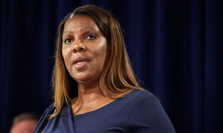 A Black woman with shoulder-length brown hair with highlights and wearing a navy top or dress speaks as she stands before a dark blue background curtain.