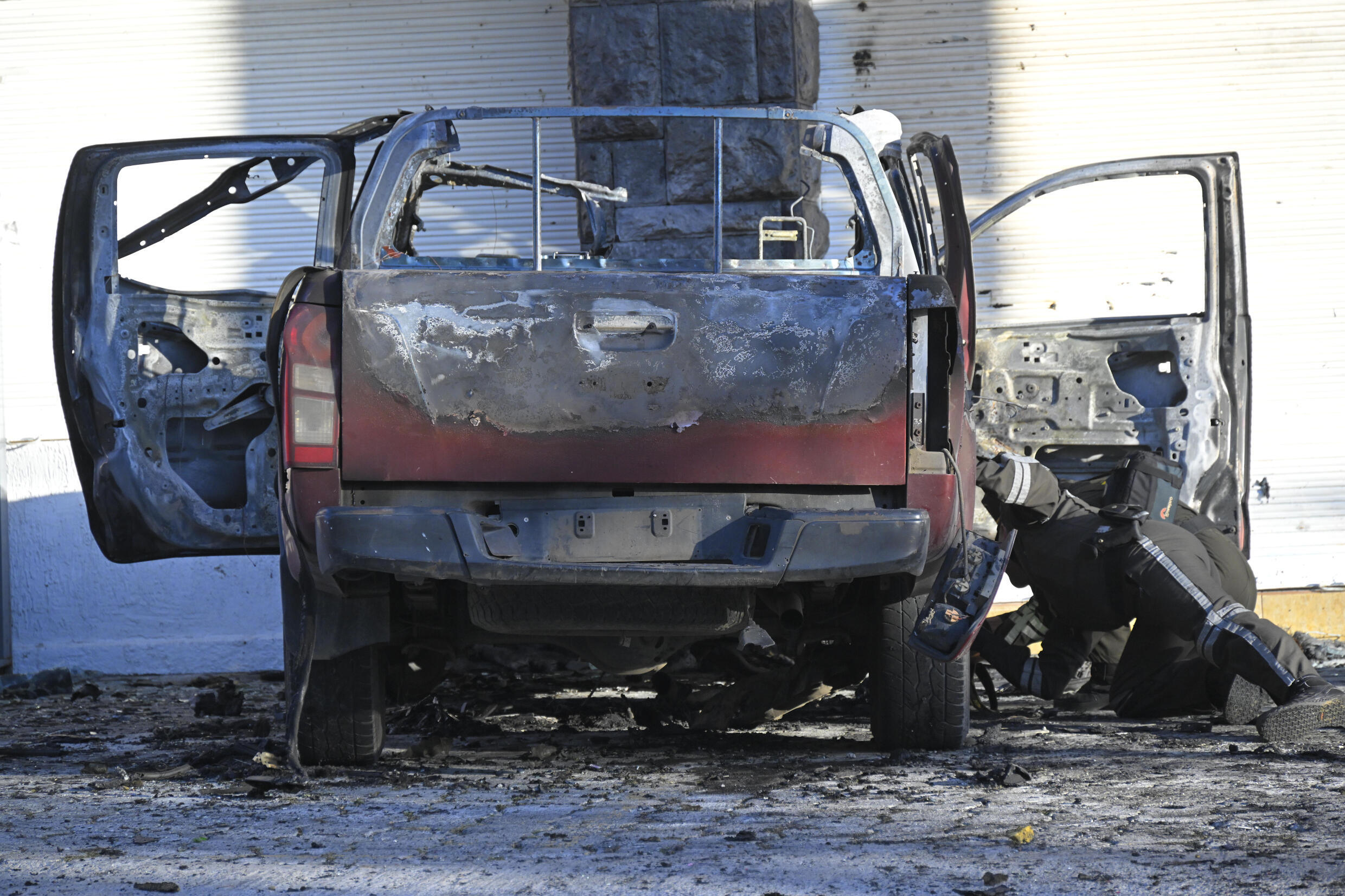 Police inspect the wreckage of a burned car in front of SNAI headquarters in Quito