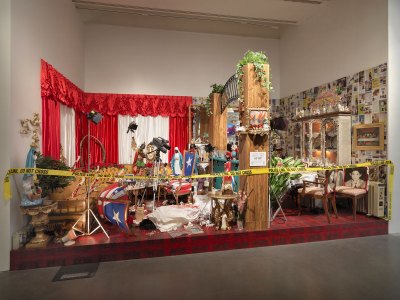 An installation work showing a Bronx apartment where a murder has taken place and is now a crime scene. It is decorated with various signifiers of Puerto Rican culture. 