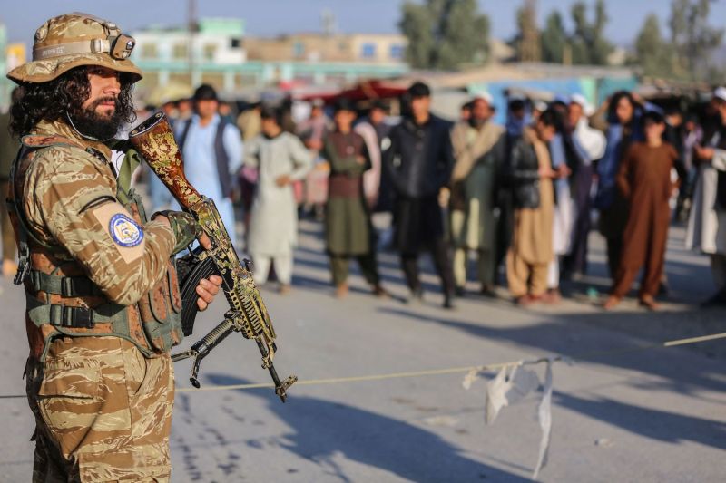 A Taliban security personnel stands guard as Afghan people wait to cross into Pakistan.