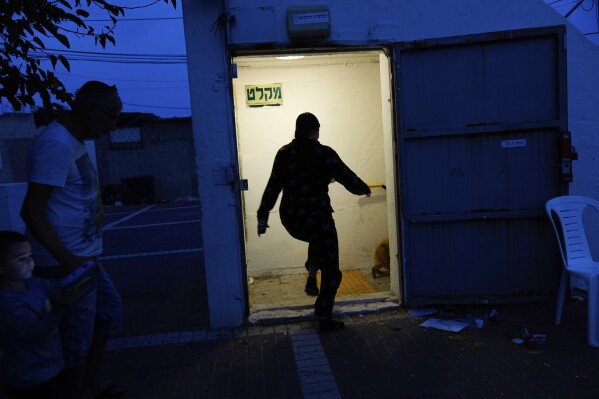 Israelis run to take cover in a shelter as a siren sounds a warning of incoming rockets fired from the Gaza strip, in Ashkelon, Israel, Sunday, Oct. 8, 2023. The militant Hamas rulers of the Gaza Strip carried out an unprecedented, multi-front attack on Israel at daybreak Saturday, firing thousands of rockets as dozens of Hamas fighters infiltrated the heavily fortified border in several locations, killing hundreds and taking captives. Palestinian health officials reported scores of deaths from Israeli airstrikes in Gaza. (AP Photo/Ohad Zwigenberg)