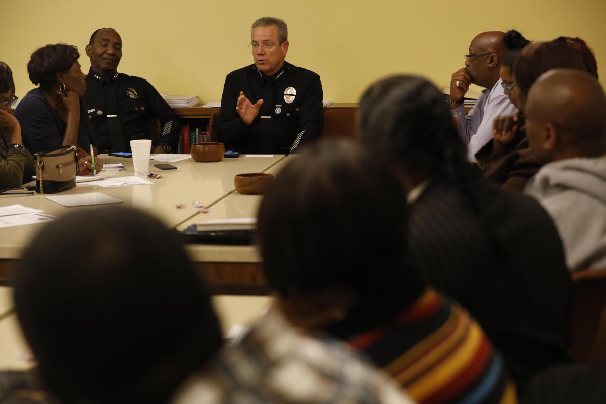 A man in a police uniform speaks to people seated around a table.