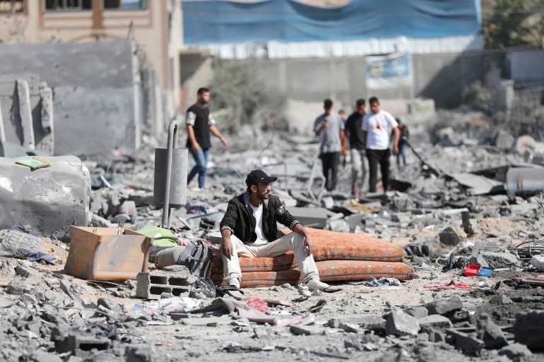 Palestinians walk by the buildings destroyed in the Israeli bombardment on al-Zahra, on the outskirts of Gaza City