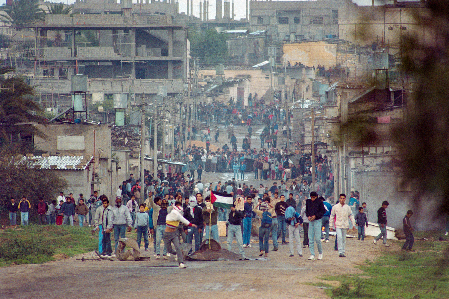 Youths plant a Palestinian flag in the street and throw rocks in Gaza during violent demonstrations during the First Intifada.