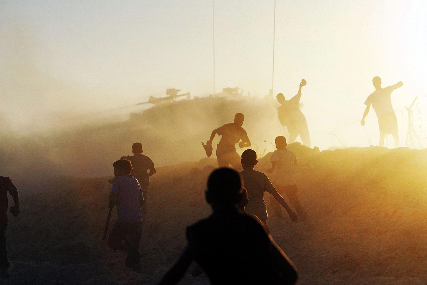 Palestinian youth throw stones toward an Israeli tank near the fence separating the southern Gaza Strip town of Khan Yunis and the Israeli settlement of Ganei Tal.