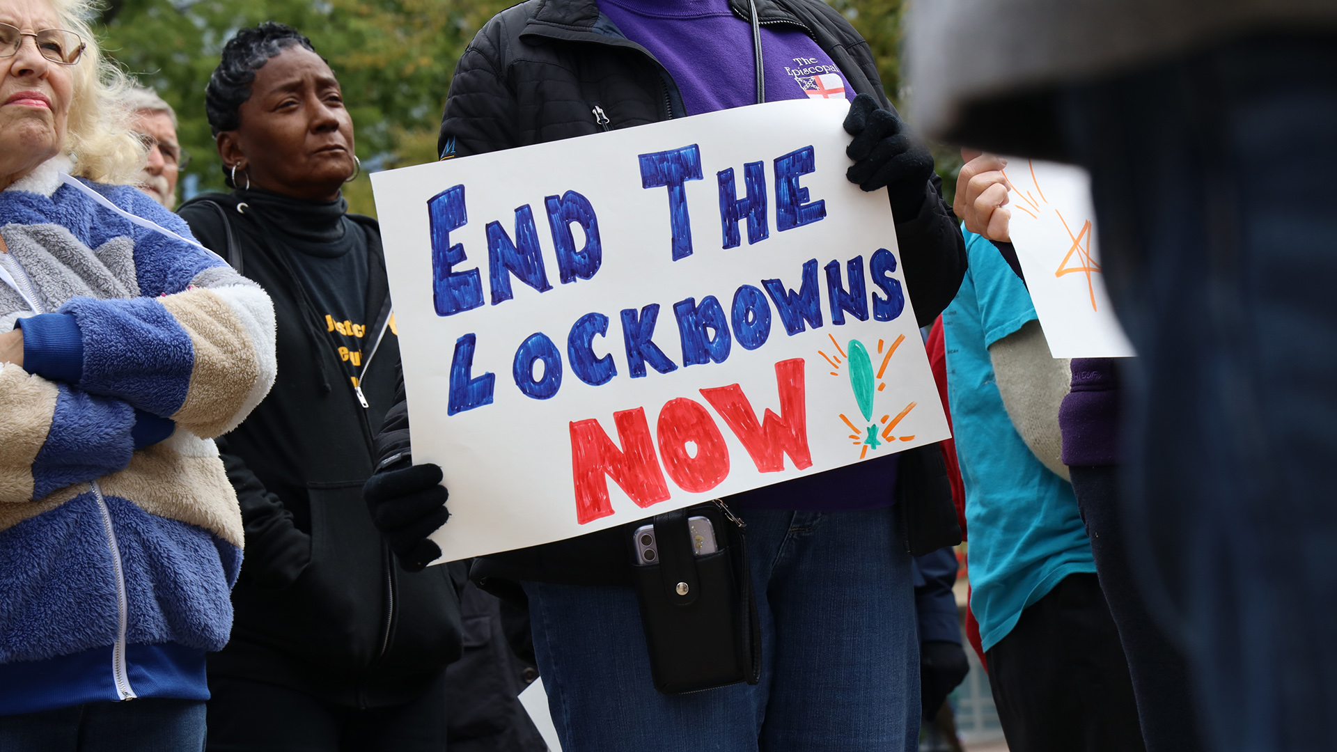 A person holds a hand-drawn sign reading 