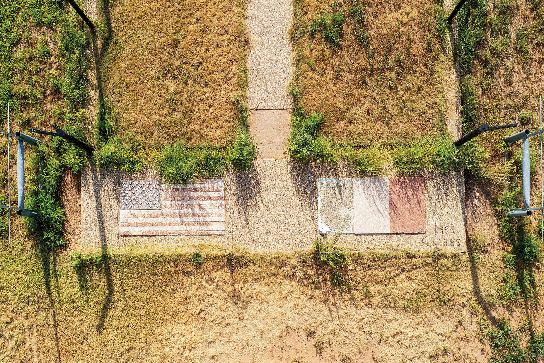 An overhead view of a field, where two large concrete markers are painted with a United States and Italian flag