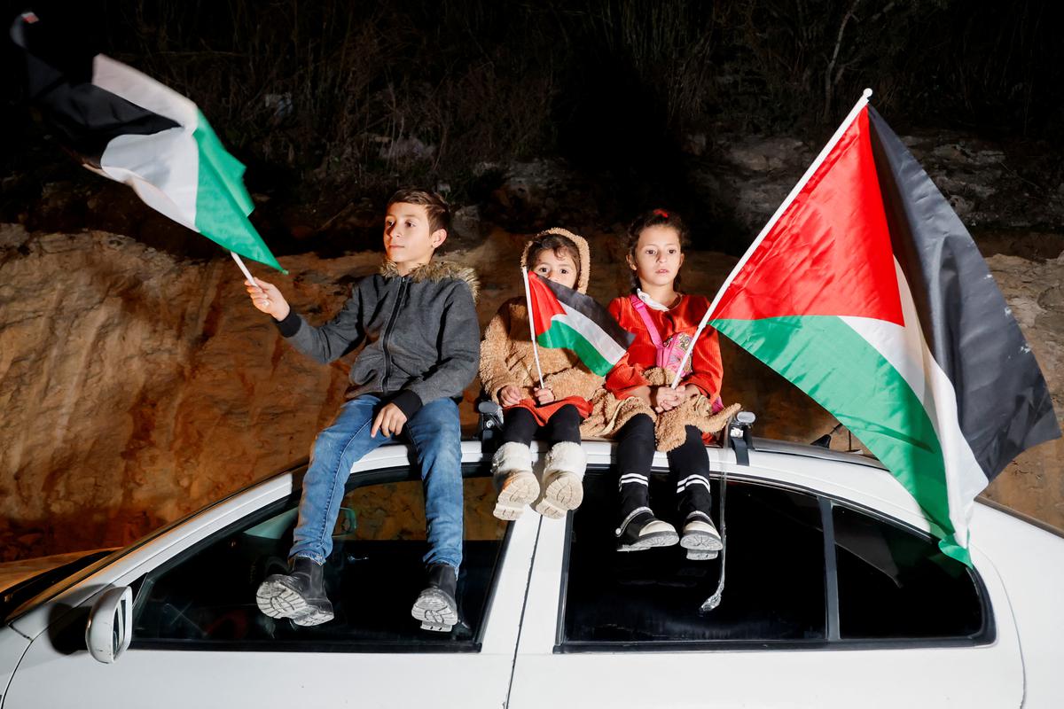 Children hold Palestinian flags sitting atop a car as family members welcome released Palestinian prisoner Fatima Amarneh, amid a hostages-prisoners swap deal between Hamas and Israel, near Jenin in the Israeli-occupied West Bank on November 25, 2023. 