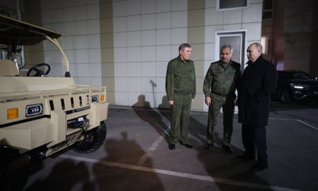 Russian president Vladimir Putin, accompanied by defence minister Sergei Shoigu and chief of the general staff of the Russian armed forces, Valery Gerasimov stand next to a desert buggy. 