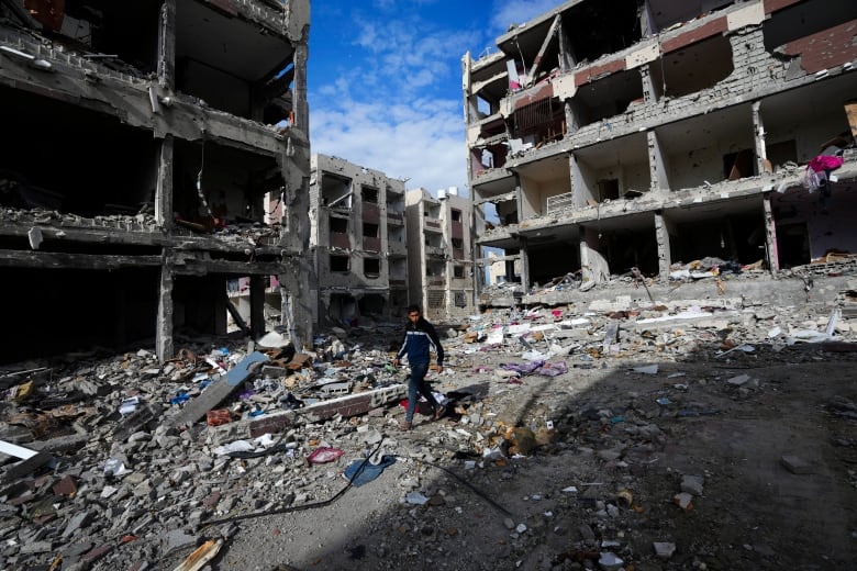 A person walks amid the rubble of destroyed buildings.