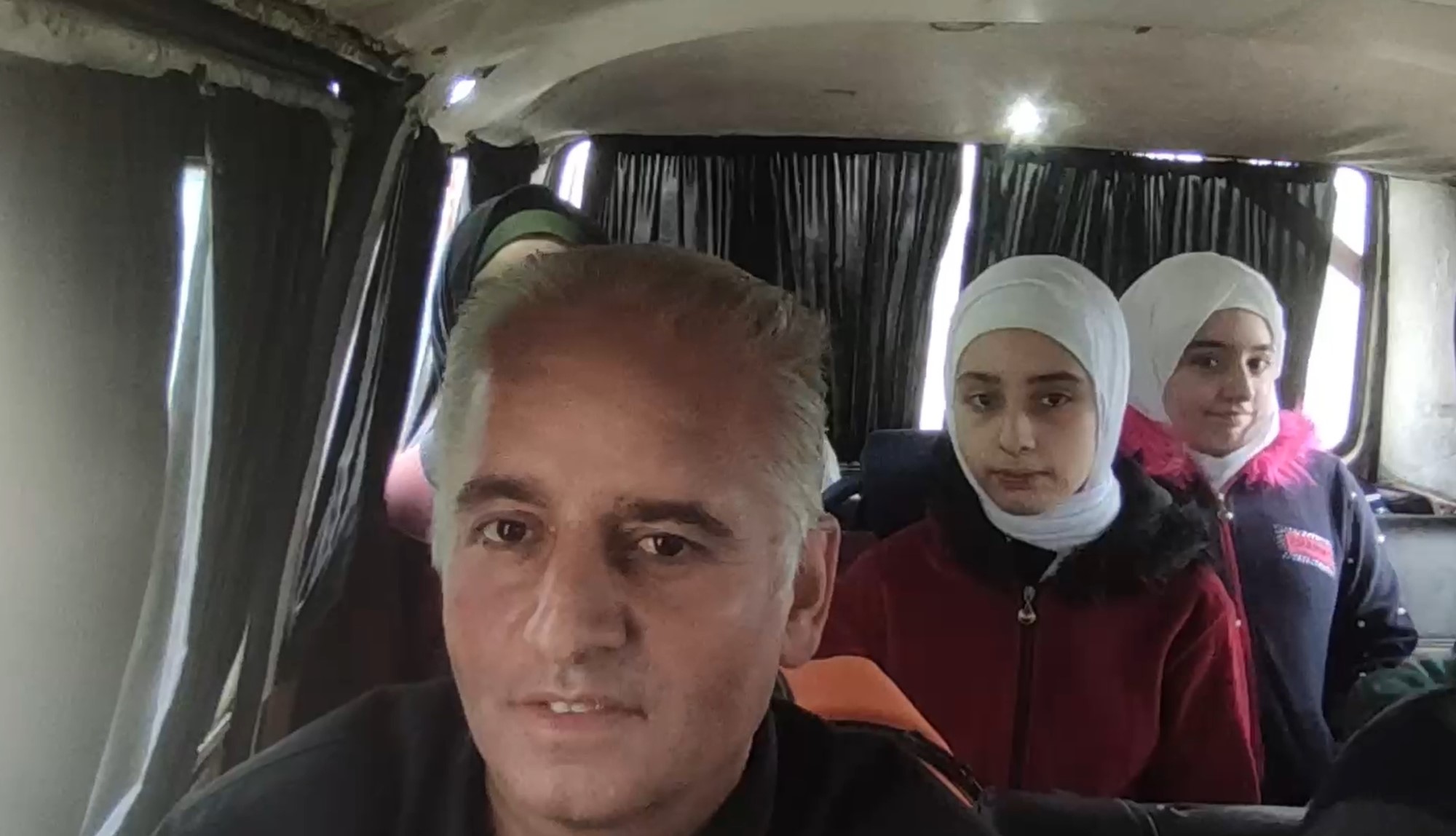 A man, and two young girls, sitting in a car, look at the camera.