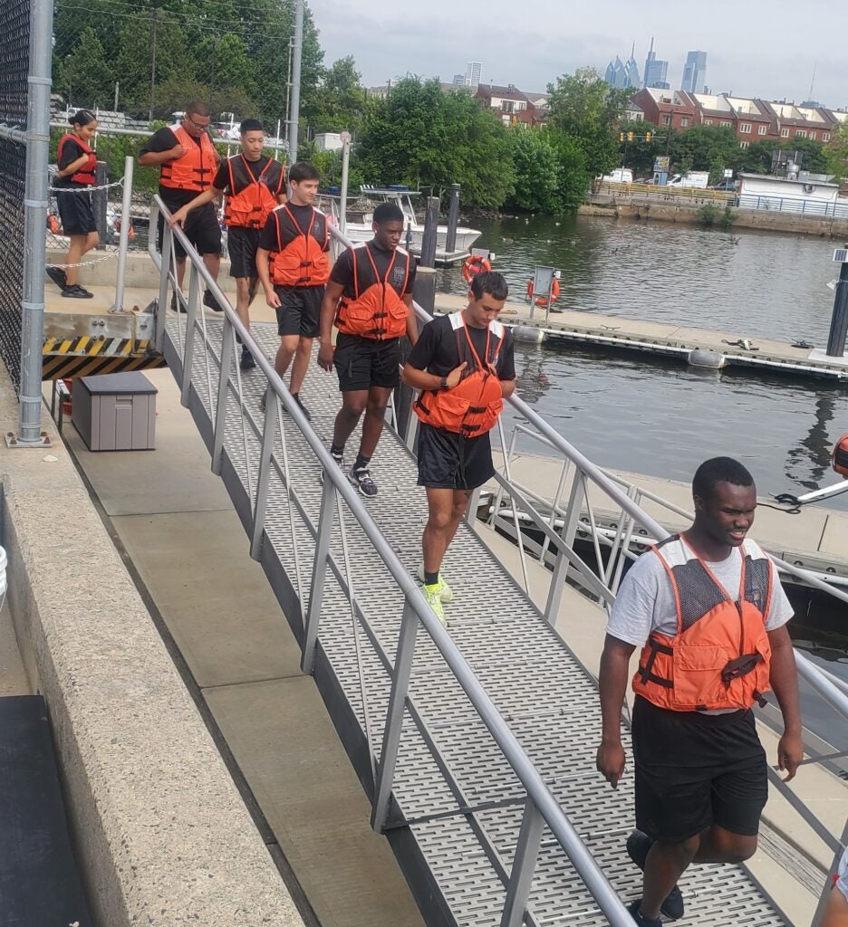 people walking along a pier wearing orange vests.