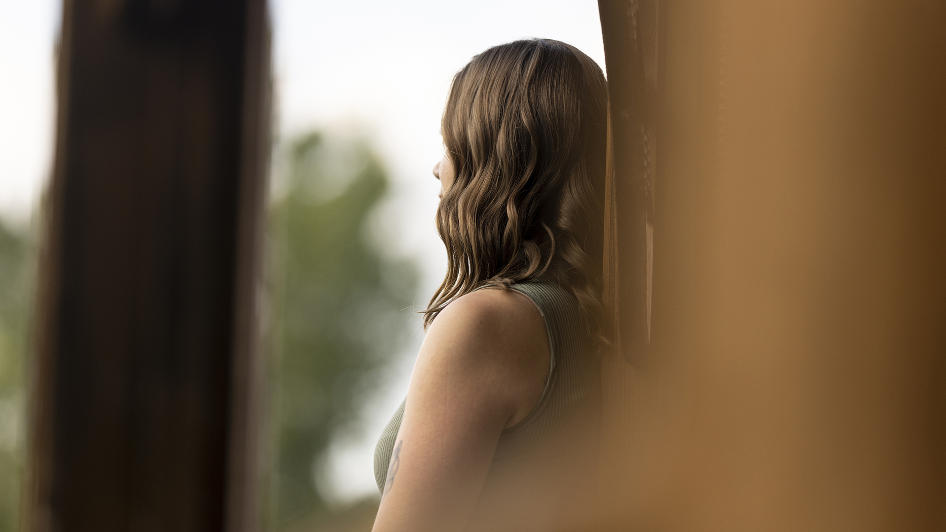 A woman faces away from a camera while leaning against a structural support of a building.