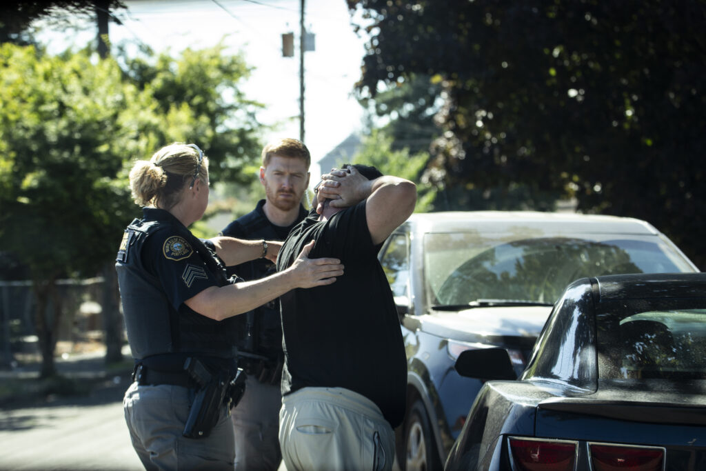 Police officers pat down a man suspected of buying sex outside his car