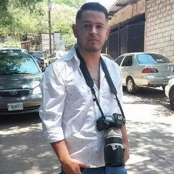 Marcel Orsoto in a white shirt with a camera dangling from his neck