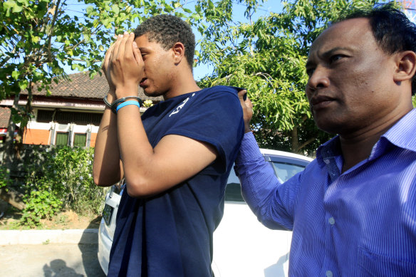 An Indonesian police officer escorts Tommy Schaefer to the police station in 2014.