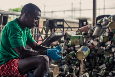 A black man wearing plastic gloves sorts cans for recycling