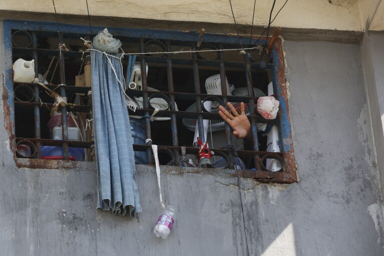 An inmate waves at the National Penitentiary in Port-au-Prince, Haiti, Sunday, March 3, 2024. Hundreds of inmates have fled Haiti's main prison after armed gangs stormed the facility overnight. (AP Photo/Odelyn Joseph)