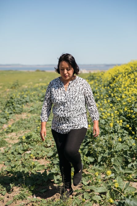 Woman wearing patterned shirt and black pants walks in green field