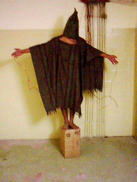 A famous image: what appears to be a man stands on a box with a black bag over his head and a black poncho, with his arms outstretched and wires seemingly attached to him.