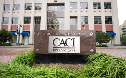 A metal placard with the name of the building on what looks like a red granite cube, in front of a multistory office building.