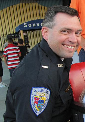 Sandra Birchwood justice: headshot of smiling man with graying dark hair in black police uniform with police department patch on upperright sleeve