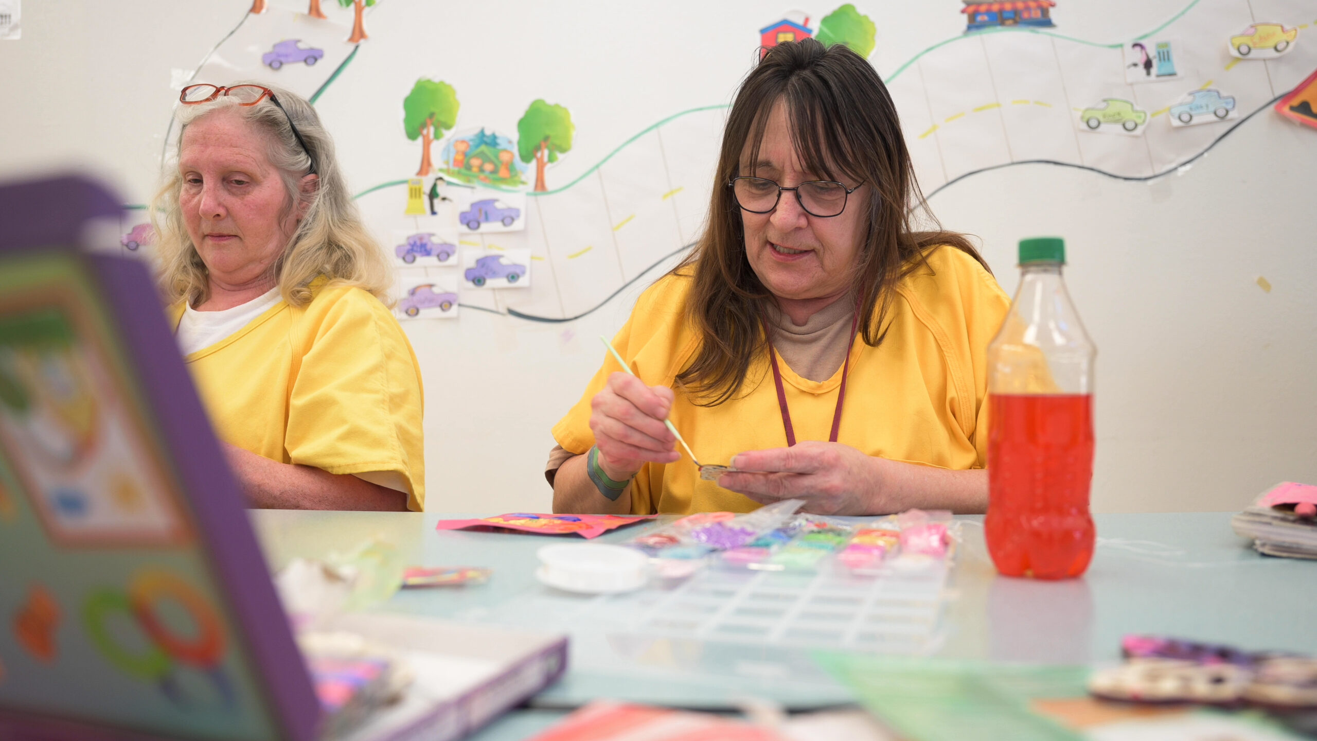 A woman in yellow sits and paints a cardboard flower.