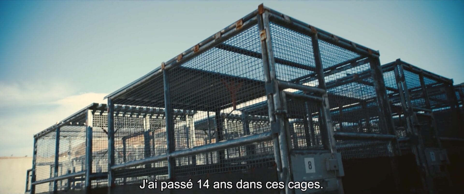 a still from a documentary in a prison in California showing chainlink cages. a French subtitle translates to 