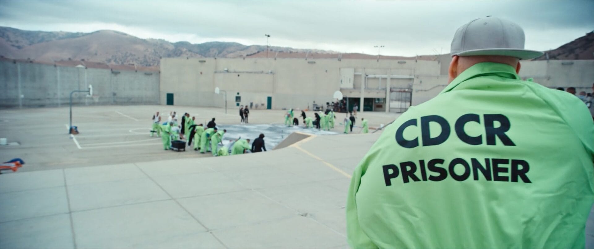 a still from a documentary in a prison in California showing inmates working on installing a large mural of portraits of themselves in the prison yard