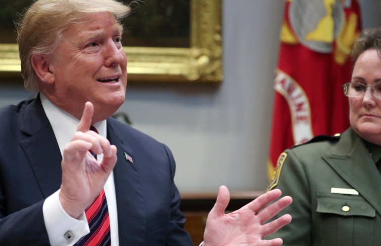 Donald Trump gestures with both hands at a table with advisors in the White House.