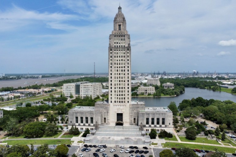 Louisiana's capitol building, a large, white-stone and concrete building with a large tower protruding in the center. Behind the building is a pond.