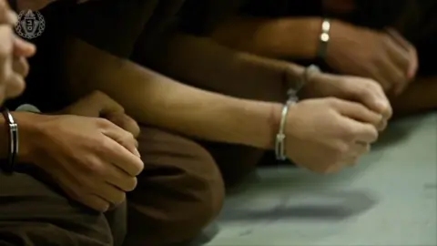 Israeli Prison Service Handcuffed hands sit in laps of prisoners sat in a row