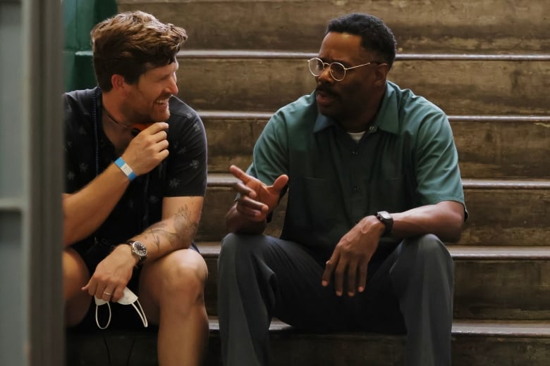 Director Greg Kwedar and actor Colman Domingo on the set of Sing Sing sittig on benches. 