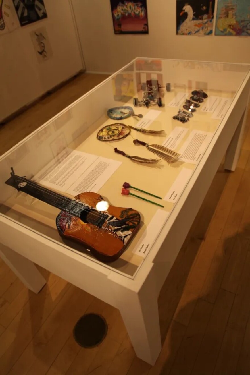 The guitar on the left is made of cardboard that Ian Cooke scrounged from legal pads. He sent it to his mother, Linda Cusano, who added the painted images on the outside.