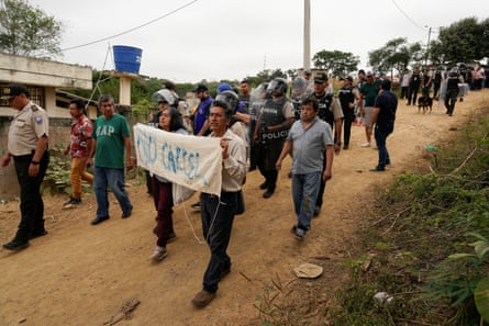 Latino people holding a banner walk along a dirt road followed by police 