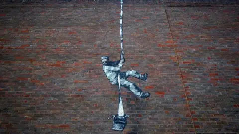 PA Artwork, created by Banksy, of a prisoner climbing down the prison wall using a typewriter 