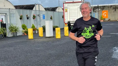 Deputy governor Alan Platt running. He has silver hair wearing a black tracksuit.