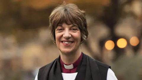 PA Media The Bishop of Gloucester, the Right Reverend Rachel Treweek, looks at the camera, smiling, with short, dark hair and with the typical clergy dog-collar and robe round her shoulders.