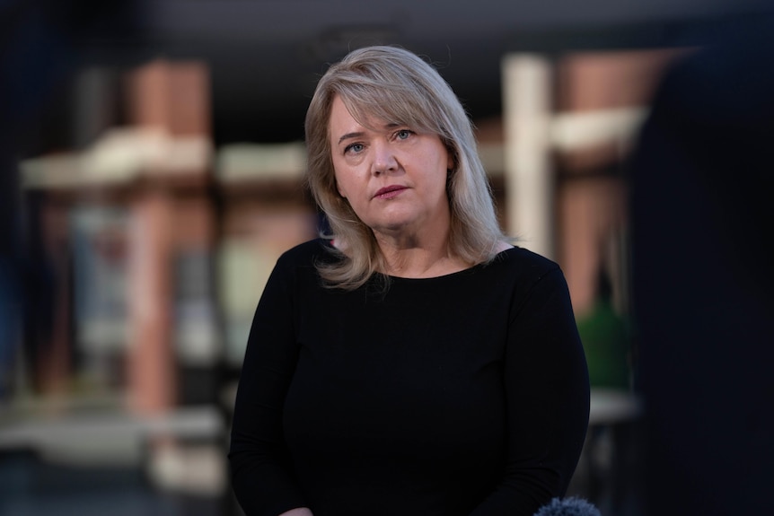 A woman with blonde hair stands in front of a building